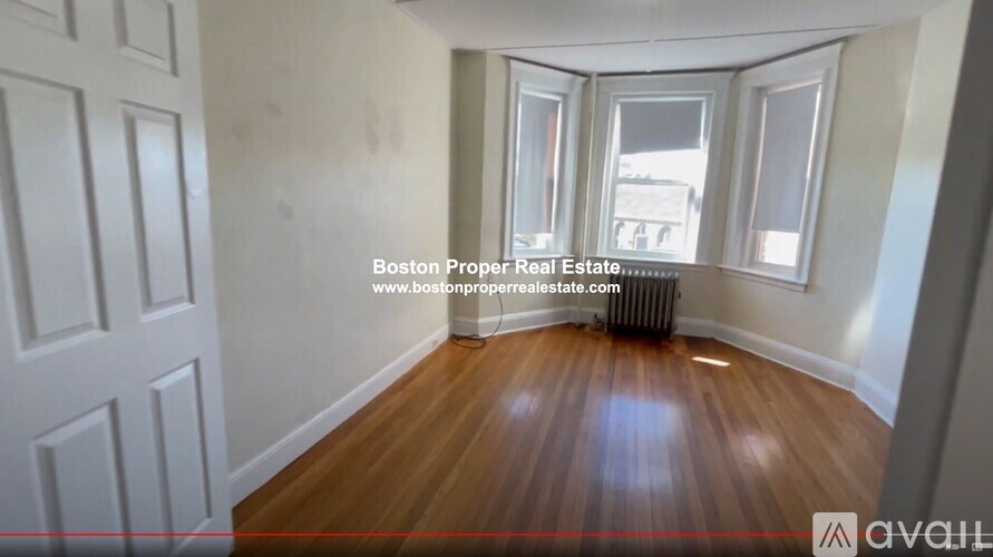 A room with wooden floors and white walls, with a window and a door visible.