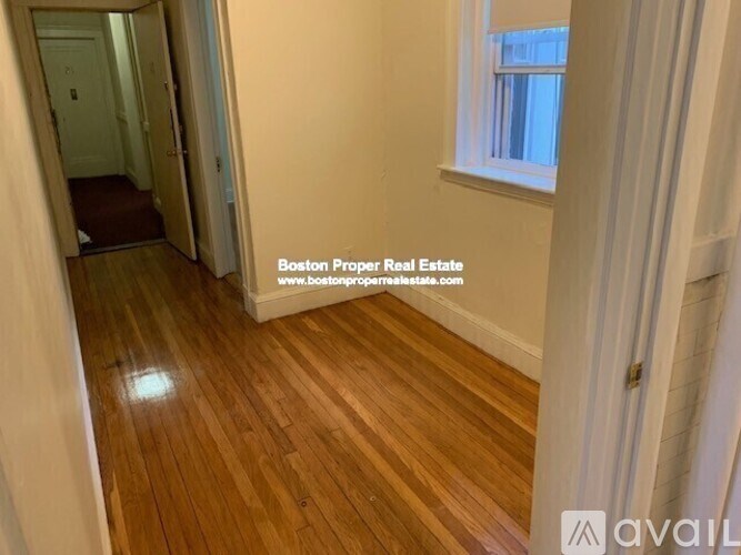 A room with wooden flooring and a window with white curtains.