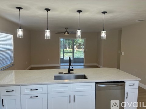 A kitchen with white cabinets and a large island with pendant lights hanging above it.
