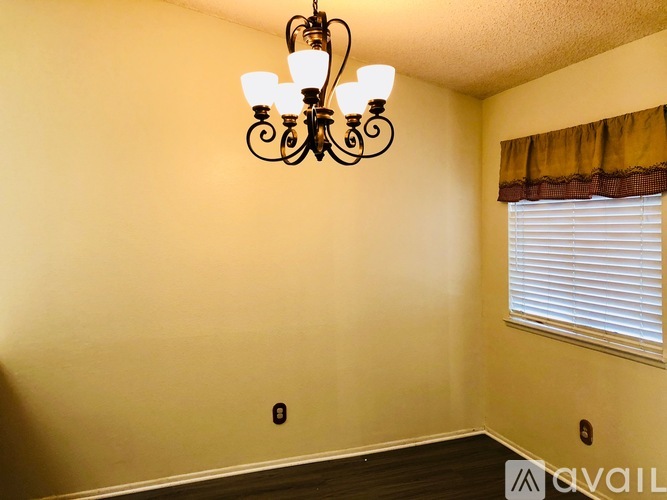 A chandelier hangs over a window in a room with a yellow wall.