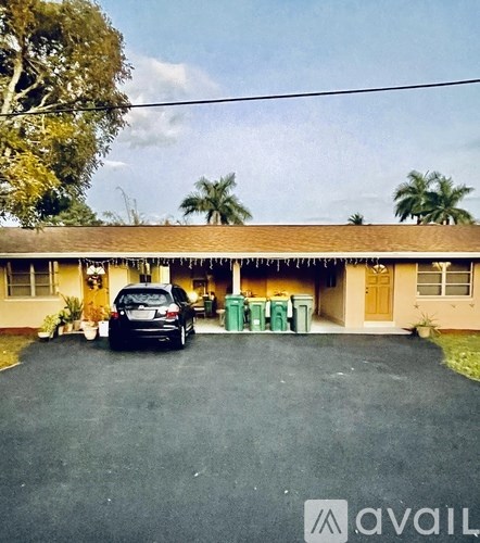 A house with a car parked in front and a green trash bin on the porch.