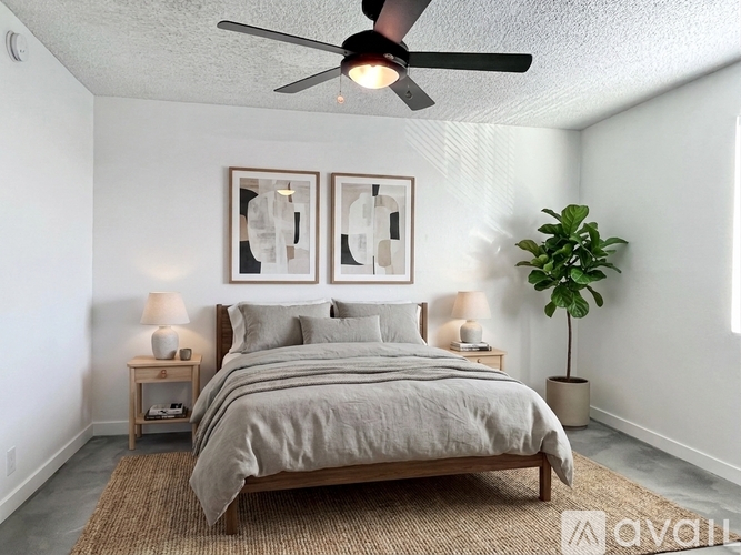 A bedroom with a bed, two lamps, a ceiling fan, and a plant.