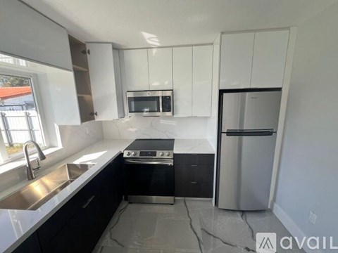 A kitchen with black and white cabinets, a stove, a microwave, and a refrigerator.
