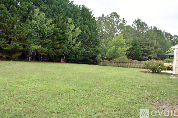 A grassy field with trees and a fence in the background.