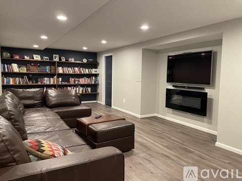 A living room with a brown leather couch, a bookshelf filled with books, a flat screen TV, and a fireplace.
