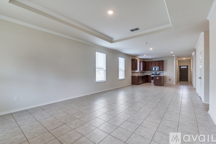A spacious living room with tiled flooring and a kitchen area in the background.