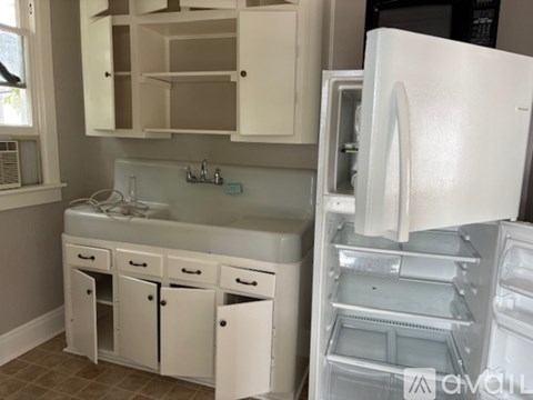 A white refrigerator is open in a kitchen with white cabinets and a sink.