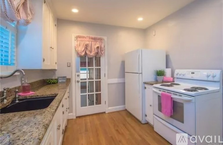 A kitchen with a granite countertop and a window with a pink curtain.