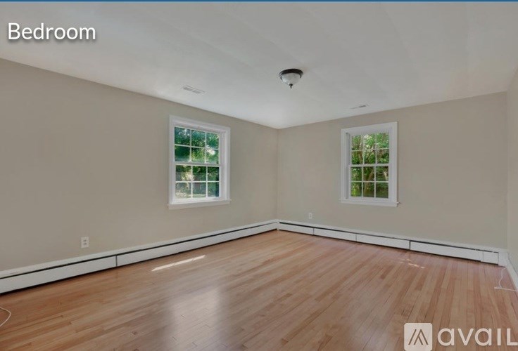 A bedroom with wooden floors and two windows.