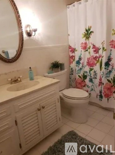 A bathroom with a floral shower curtain and a round mirror above the sink.