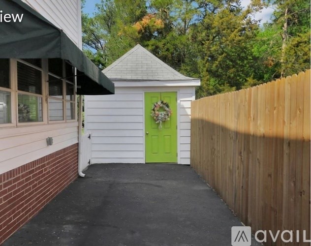 A small white shed with a green door is situated next to a wooden fence.