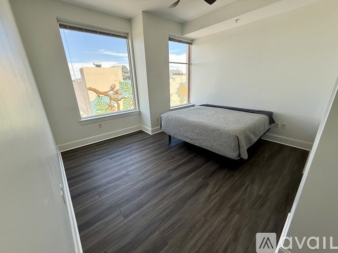 A bedroom with a bed, wooden floors, and a window with a view of a building.