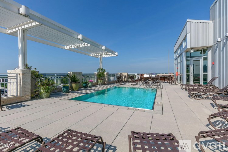 A pool area with a white pergola and brown lounge chairs.