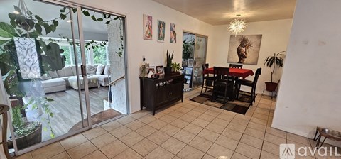 A living room with a dining table and chairs, a potted plant, and a painting on the wall.