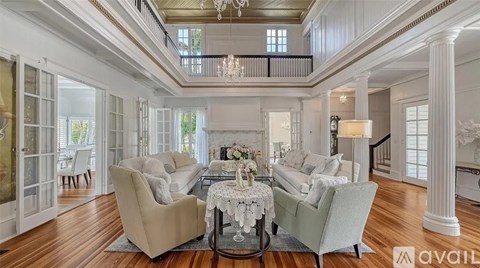 A spacious living room with a dining table set in the middle and a chandelier hanging from the ceiling.