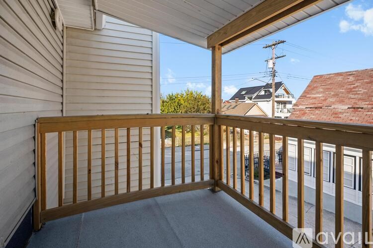 A balcony with a wooden railing and a view of a house and trees.