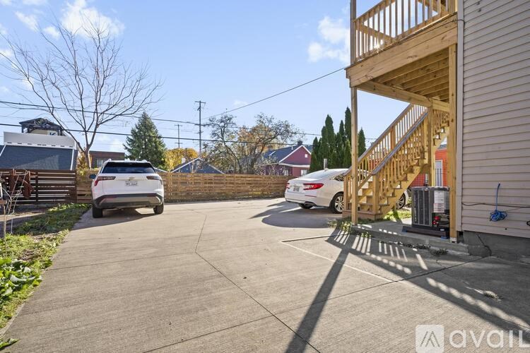 A white car is parked in a driveway with a wooden staircase leading to a house.