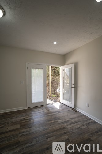 A room with wooden floors and two open doors leading outside.