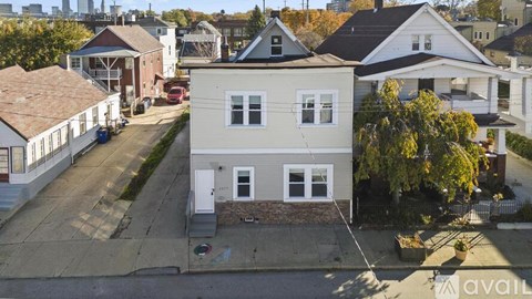 A house with a grey front and a white door is in the foreground of a street with other houses in the background.