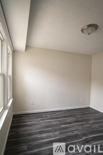 A room with a wooden floor and a window on the left side.