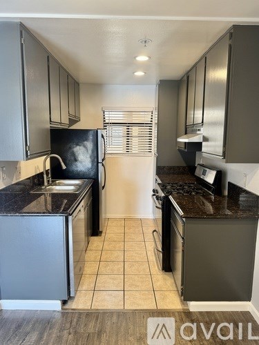 A kitchen with a black fridge, black countertops, and a black stove top oven.