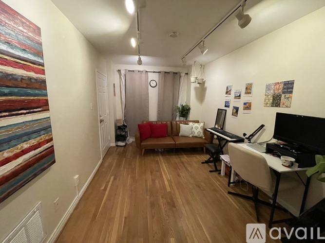 A living room with a couch, a television, a desk, and a painting on the wall.