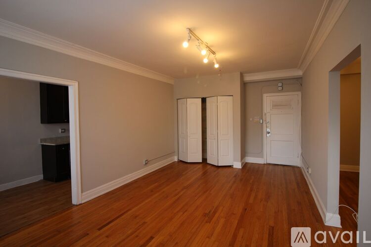 A room with wooden floors and white walls, with a small window on the left and a door on the right.