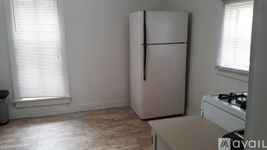 A white fridge in a kitchen with a stove and a window with blinds.