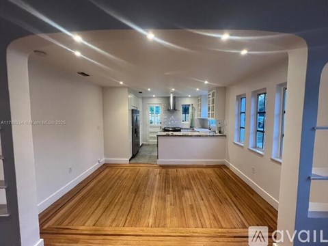 A spacious room with wooden floors and a kitchen area in the background.