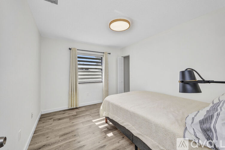 A bedroom with a bed, a window with curtains, and a lamp.