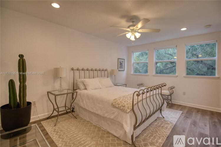 A bedroom with a bed, a cactus, and a ceiling fan.