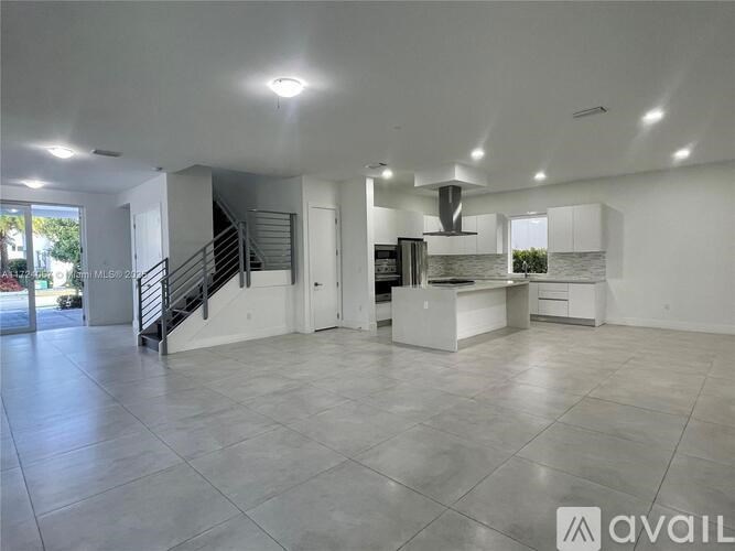 A spacious, empty room with a staircase and a kitchen area.