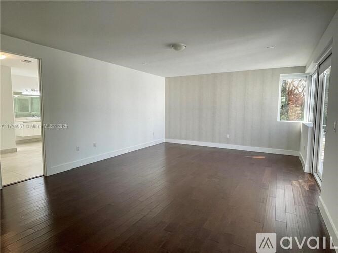 A spacious room with wooden flooring and white walls.