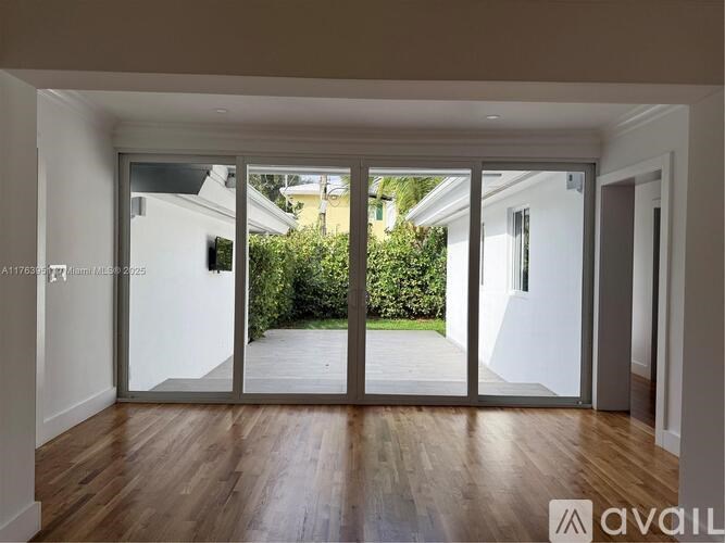 A spacious room with wooden floors and a view of a garden through the glass doors.