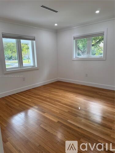 A room with wooden flooring and two windows.