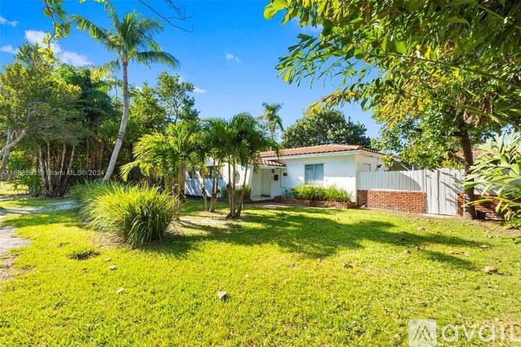 A house with a white fence and a green lawn is surrounded by trees.
