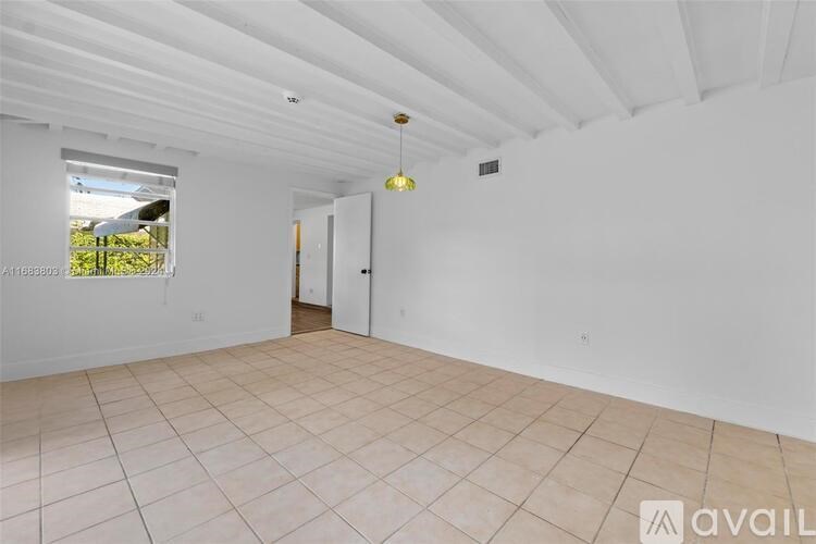 A spacious room with a tiled floor and a window overlooking a green area.
