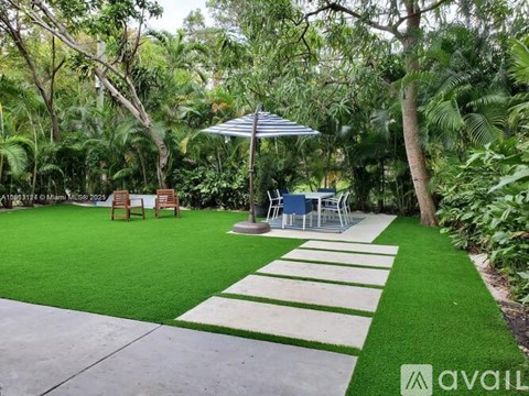 A patio with a white and green striped rug, a white umbrella, and a white table with chairs.
