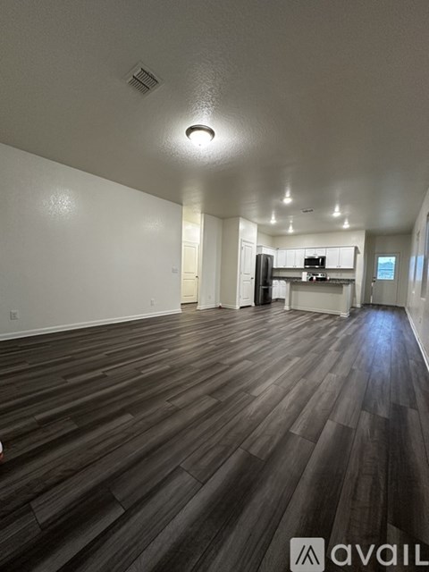 A spacious room with wooden flooring and a kitchen area in the background.