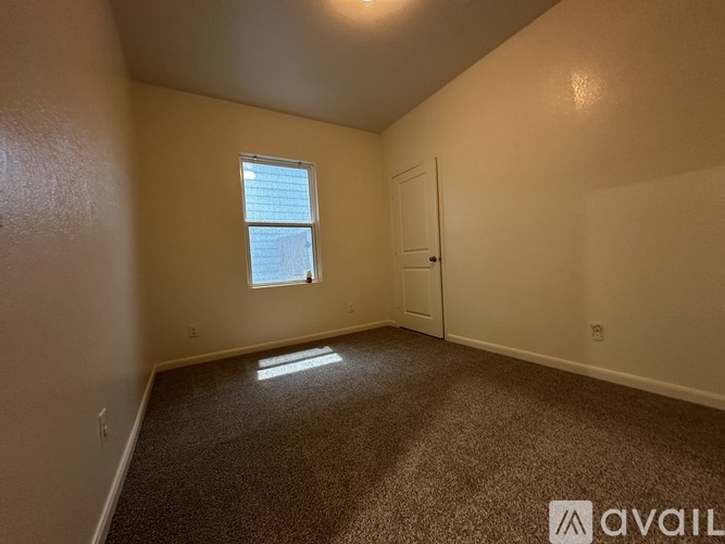 A room with a carpeted floor, a window, and a door.
