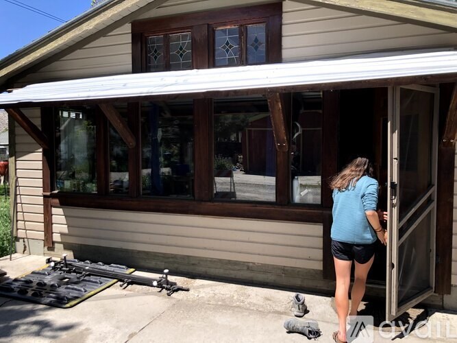 A woman in a blue shirt and black shorts is entering a house.