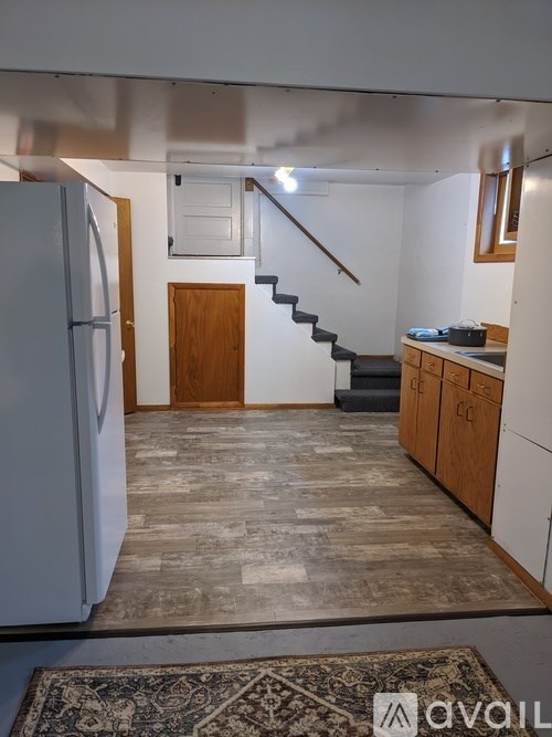 A kitchen with a refrigerator, stairs, and cabinets.