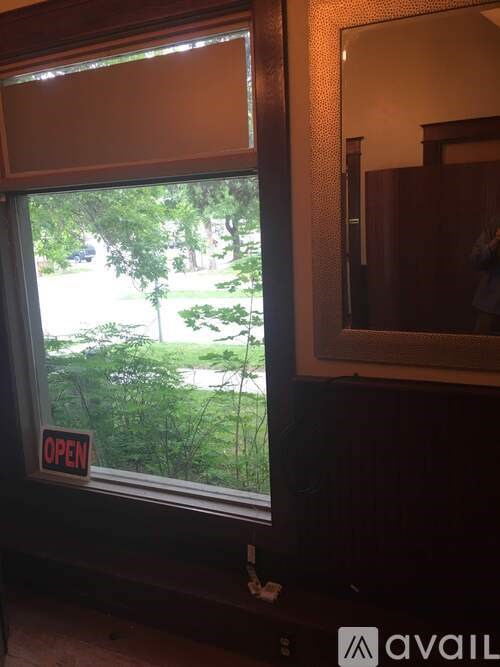 A window with a sign that says "OPEN" is open to a view of a green outdoor area.