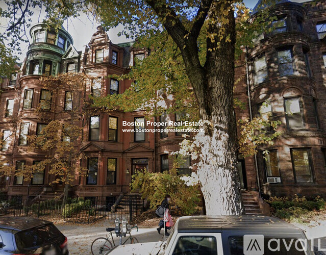 A tree in front of a brown building with a car parked in front of it.
