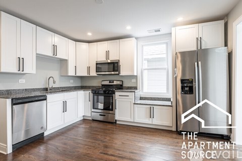 A well-lit, modern kitchen with stainless steel appliances and wooden floors.
