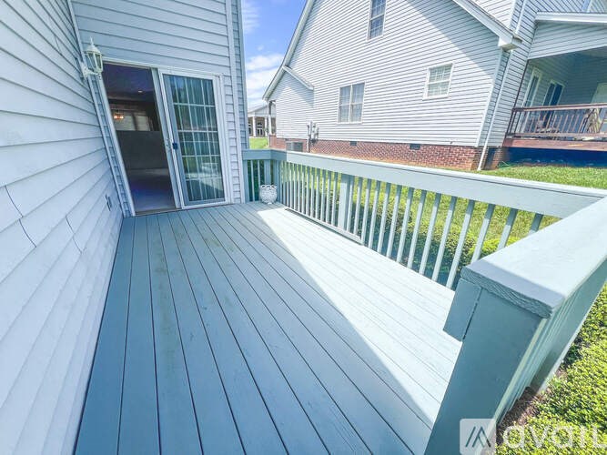 A wooden deck with a white railing and a glass door leading to a house.