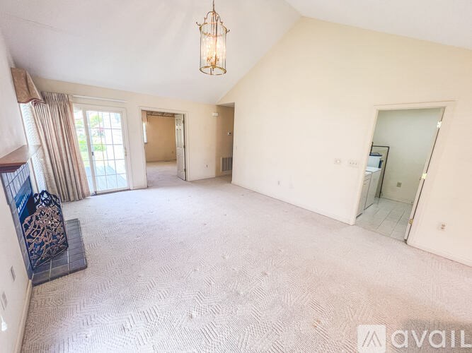 A spacious room with a carpeted floor, a chandelier, and a mirror on the wall.