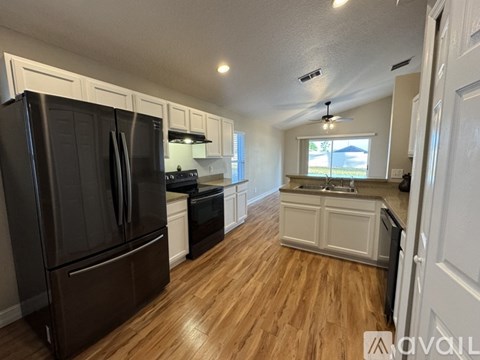 A kitchen with a black refrigerator and wooden floors.