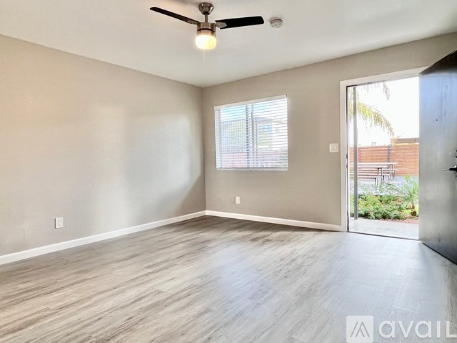 A room with a ceiling fan and light, wooden flooring, and a window with blinds.