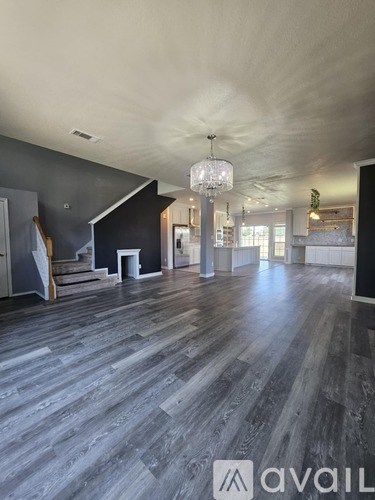 A spacious room with wooden flooring and a chandelier hanging from the ceiling.